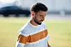 Bruno Fernandes går utendørs i sollys med en hvit og oransje genser foran en uskarp bakgrunn.