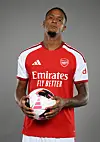 Fotballspiller i Arsenals røde drakt holder en fotball foran en grå bakgrunn.