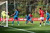 Fotballspillere i røde og blå drakter kjemper om ballen foran mål på en treningsbane.
