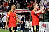 To belgiske fotballspillere i røde drakter feirer foran tilskuere på tribunen.
