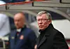 Sir Alex Ferguson står i svart frakk på en fotballarena, med en uklar person i Manchester United-antrekk i bakgrunnen.
